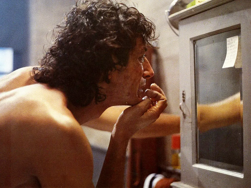 Close-up of a person with curly hair leaning against a window while smoking.